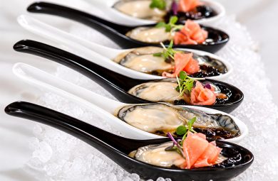 Fresh oyster canapés presented on black and white tasting spoons